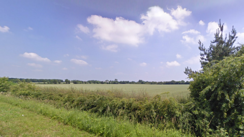 A hedgerow and then green fields, with Hanwell in the distance 