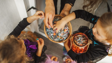 An image of children grabbing sweets in a bowl at Halloween.