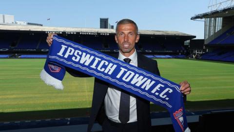 Gary O'Neil holds a Ipswich Town scarf while wearing a suit stood inside Portman Road
