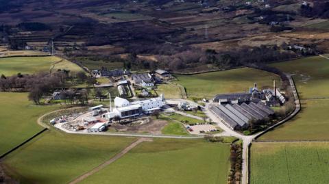 An aerial view of Clynelish Distillery in Brora. The distillery is made up of a number of large buildings and is is set in a rural landscape of fields.