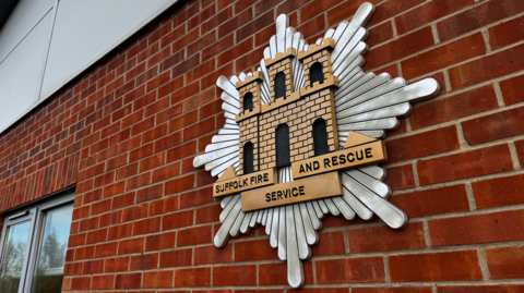 A large Suffolk Fire and Rescue Service emblem on the side of a brick building.