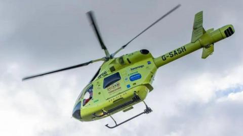Stock image of a Yorkshire Air Ambulance in the air with its propeller moving. It is a bright yellow colour and has various logos and words written on it.