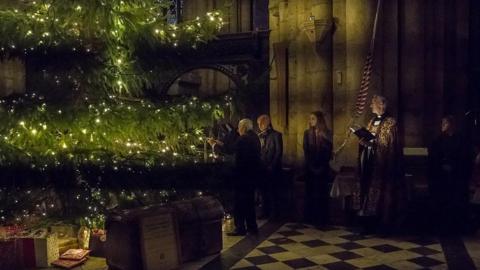 Jackie McCowliff hanging the miner's safety lamp on the tree. He has white hair and is standing next to another man, Sally Lockey who has long brown hair and the Reverend Canon.