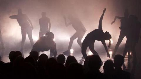 dancers silhouetted on a stage with the audience in the foreground