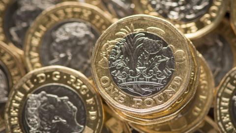 A picture of pound coins piled up. They are silver and gold in colour.