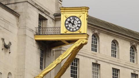 A gilded clock on Leeds Civic Hall. The clock is mounted on a hefty bracket on the east side of the building.