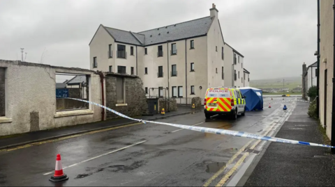 Police van and police tape on road at scene of incident among houses