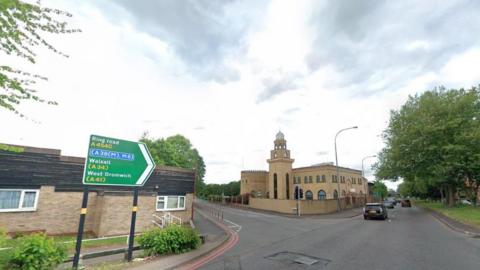 The junction of Icknield Street and Hingeston Street. There is a dual cariageway lined with trees and a central verge. On the left hand side of the photo is a green road sign.