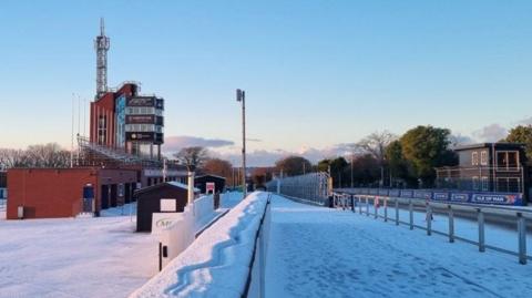 The grandstand, a large brown building, with snow around it.