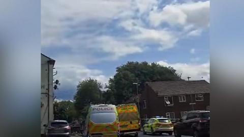 Police and ambulance vehicles at the scene of an altercation on Keb Lane, Bardsley, Oldham, on a cloudy day. 