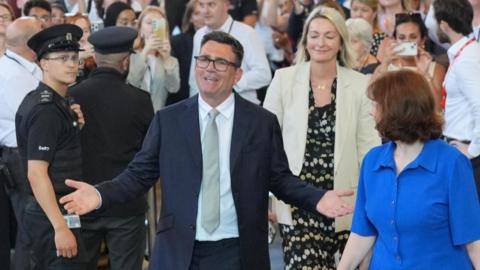 Andy Burnham opens his arms wide with MPs looking on behind him