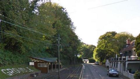 King Edward Road, which has tram tracks o the left side of the road and a white building, with an old pub next to it, there are a lot of trees on either side of the road.