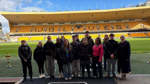 A group of teenagers in coats are stood together in the grounds of the Molineux Stadium