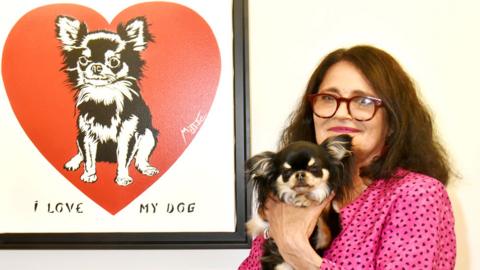 Miss. Tic poses with her dog in front one of her works in May 2018