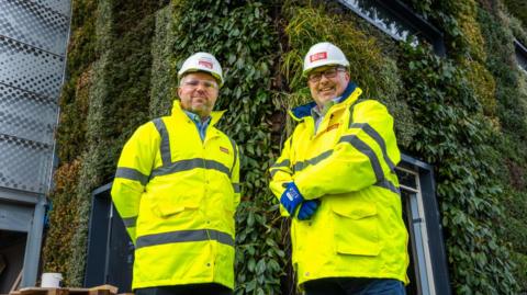 Two men in high-viz vests stand outside car park