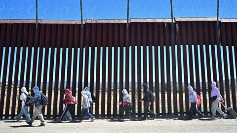 Migrants walk on the US side of the border wall in Jacumba Hot Springs, California. Photo: June 2024 