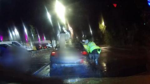 Dashcam image shows rear of car at night time with two police officers in hi-vis jackets leaning in to driver's door