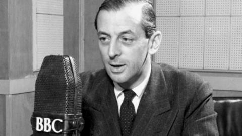 Alistair Cooke talking into a BBC microphone while wearing a suit