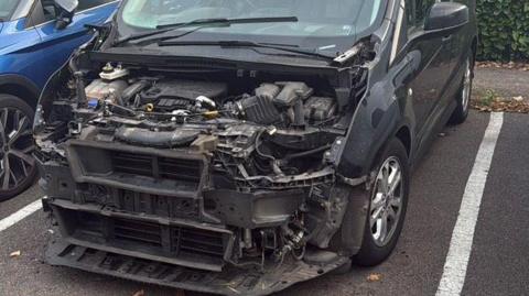 The complex interior of the front of a van, visible because everything covering it has been stripped, the dark van is parked in a bay