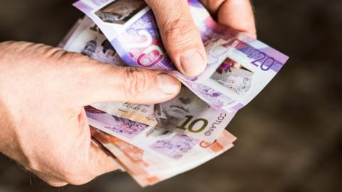 A man's hands handle a variety of Scottish bank notes