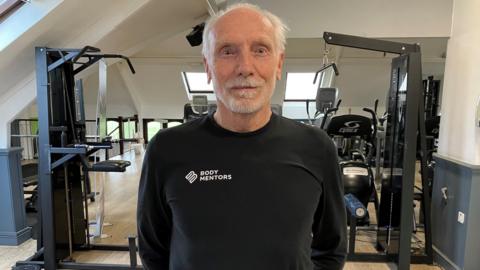 David Wallis, dressed in gym kit, looks straight into the camera in a weightlifting room.