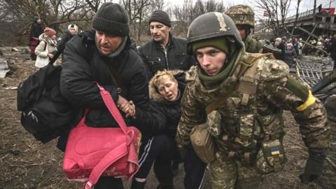 A visibly exhausted woman is assisted while crossing a destroyed bridge in the city of Irpin, northwest of Kyiv