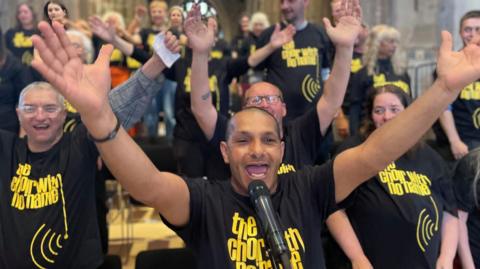 Men and woman in matching black t-shirts stand arms aloft smiling