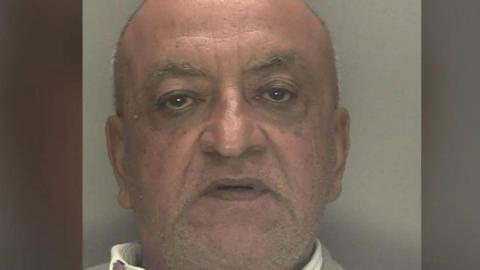 An elderly mugshot of a bald, elderly man.