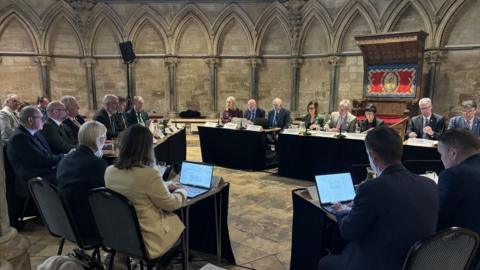 Council leaders and officials sitting at desks at the meeting inside Lincoln Cathedral's Chapter House. 