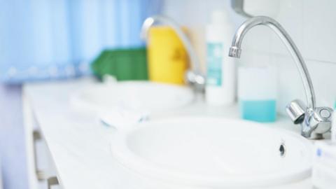 A clinical sink with a tap over it, with soap on the side of it 