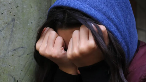 A young person holding their clenched fists up to their face