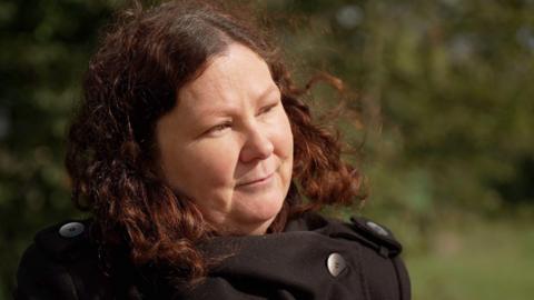 Cassandra Wardle looks off frame with a black coat in a countryside background