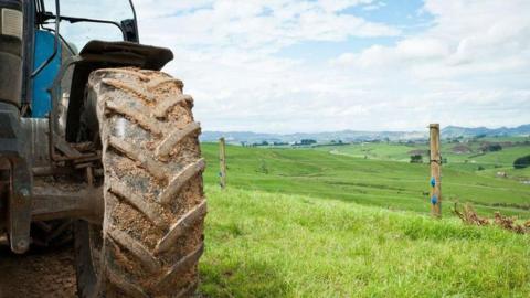 A partial picture of tractor focused on the large back wheel on the right hand side with grassy fields in the background