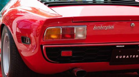 A close-up of the rear of a red Lamborghini sports car, showing the tail lights, exhaust pipe and Lamborghini badge.