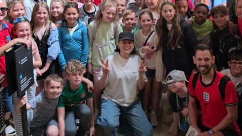 Singer Jessie J wears white t shirt, blue jeans and dark cap as she poses with many children