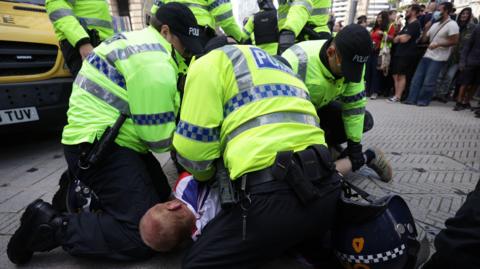 Three police officers in yellow high viz uniforms pin a man to the ground during disorder in Liverpool.