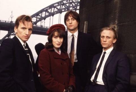 The cast of Our Friends in the North standing in front of the Tyne Bridge. ThePicture shows Christopher Eccleston as Nicky, Gina McKee as Mary, Mark Strong as Tosker and Daniel Craig as Geordie. The men are wearing dark suits with white shirts and ties and McKee is wearing a plum-coloured coat and hat