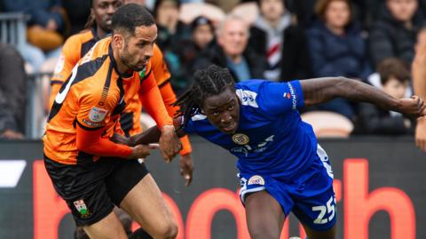 Joe Kizzi in Barnet's amber and black kit grapples with an attacker in all blue