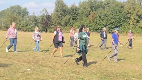 A group of people walking through a field holding Nordic walking poles.