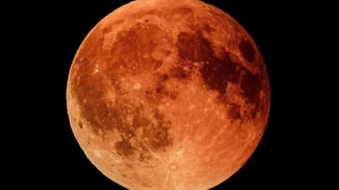The moon with a vibrant red hue with dark patches of red scattered across the moon's surface.