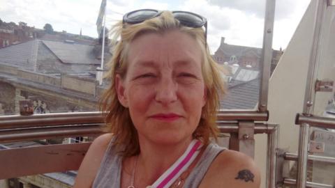 Dawn Stugess, with light coloured hair, and wearing a grey top looking into camera. She is looking into camera.