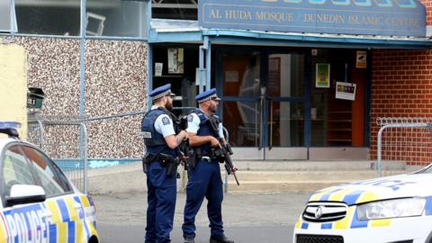 Police look on as locals lay flowers and condolences at the Huda Mosque in tribute to those killed and injured at the Al Huda Mosque