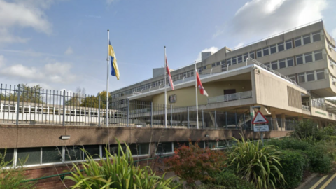 Three flagpoles outside a concrete council building. They fly the yellow and blue Ukraine flag, the Union flag and the red and white county flag