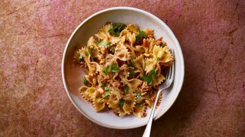 Hot harissa tuna pasta in a pasta bowl on a dark red/pink background