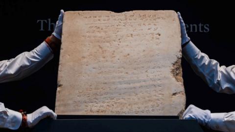 Two auction house workers hold up a tablet of the Ten Commandments in Paleo-Hebrew 