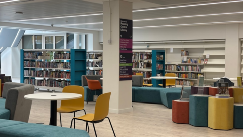 Image of a library with rows of books and yellow, blue and grey chairs and sofas. 