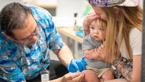 A one-year-old is held by his mother while he receives an MMR vaccine at a clinic in Texas