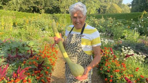 Alan Gray stood in his colourful garden holding a long tromboncino