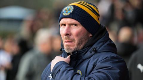 Shrewsbury Town manager Michael Appleton in his club beanie and puffer coat watches on from the touchline