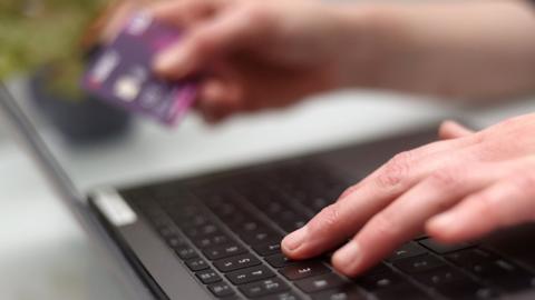 Person using laptop while holding bank card